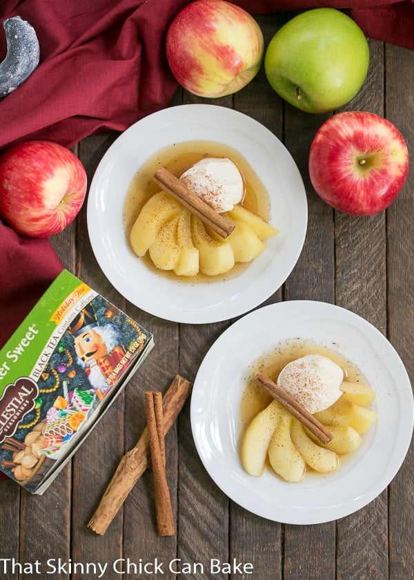 Overhead view of Tea Poached Apples on dessert plates with fresh apples, cinnamon sticks and a box of tea.