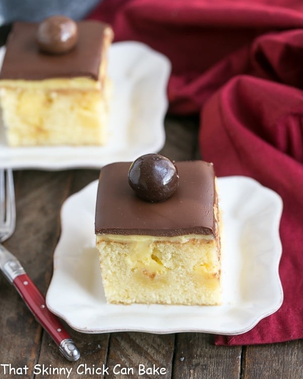 Boston Cream Pie Poke Cake combines two fantastic desserts, Boston cream pie and poke cake, into a moist, buttery cake filled with vanilla pudding and topped with chocolate ganache! 2 white dessert plates of Boston Cream Pie Poke Cake