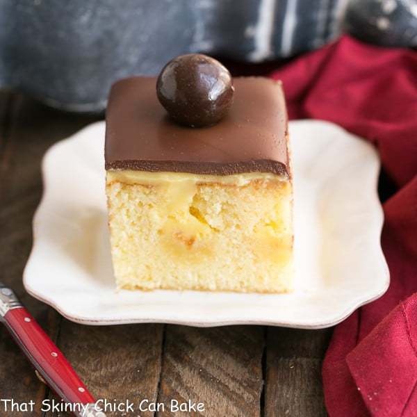 This Poke Cake Recipe combines two fantastic desserts, Boston cream pie and poke cake, into a moist, buttery cake filled with vanilla pudding and topped with chocolate ganache! Boston Cream Pie Poke Cake on a plate