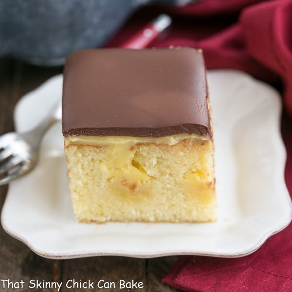 This Poke Cake Recipe combines two fantastic desserts, Boston cream pie and poke cake, into a moist, buttery cake filled with vanilla pudding and topped with chocolate ganache! piece of Boston Cream Pie Poke Cake on a white dessert plate
