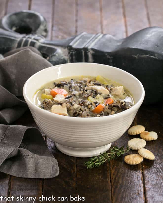 Wild Rice Soup in a white bowl with oyster crackers and a sprig of thyme.
