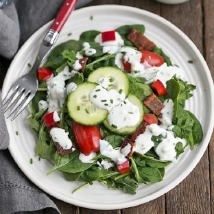Overhead view of a green salad with blue cheese salad dressing on a round white plate