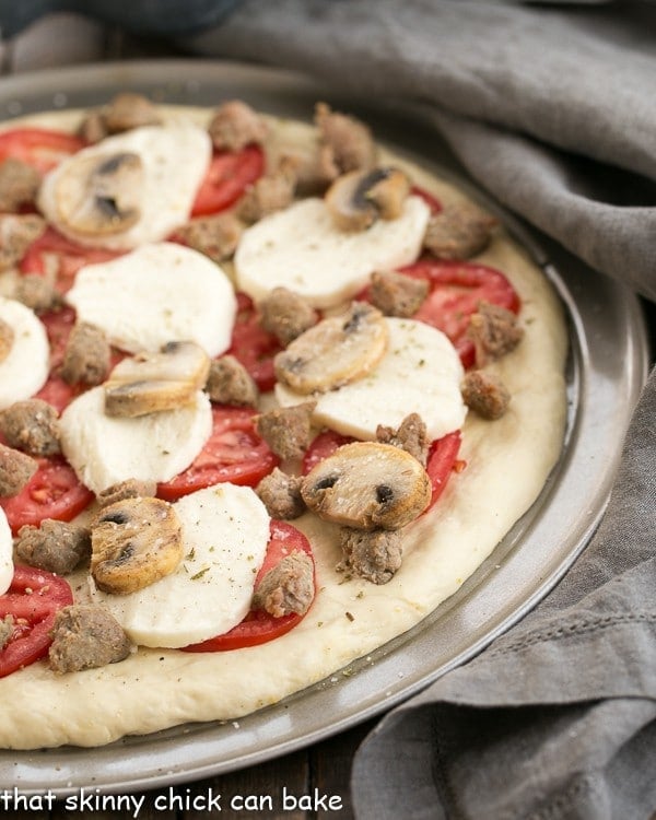 Homemade Pizza Dough make with yeast and topped with mozzarella, tomatoes, sausage and mushrooms! Sausage Mushroom Pizza on a pizza pan ready for the oven.
