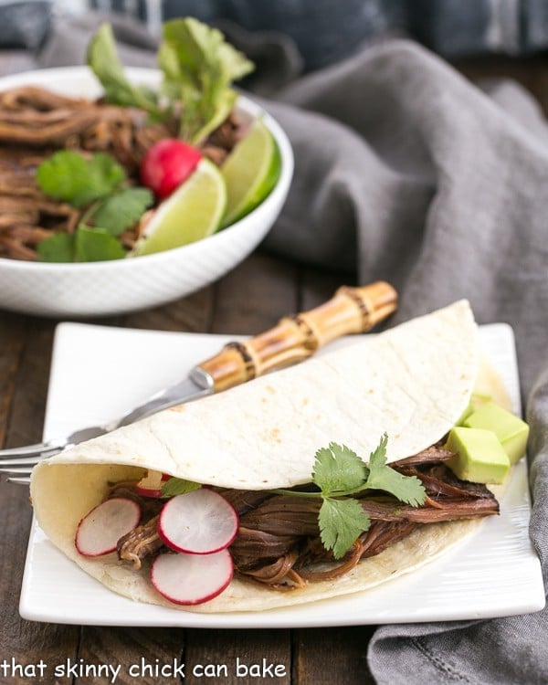 Slow Cooker Carne Asada - The classic Latin dish made in a slow cooker! Slow Cooker Carne Asada in a tortilla on a square white plate.