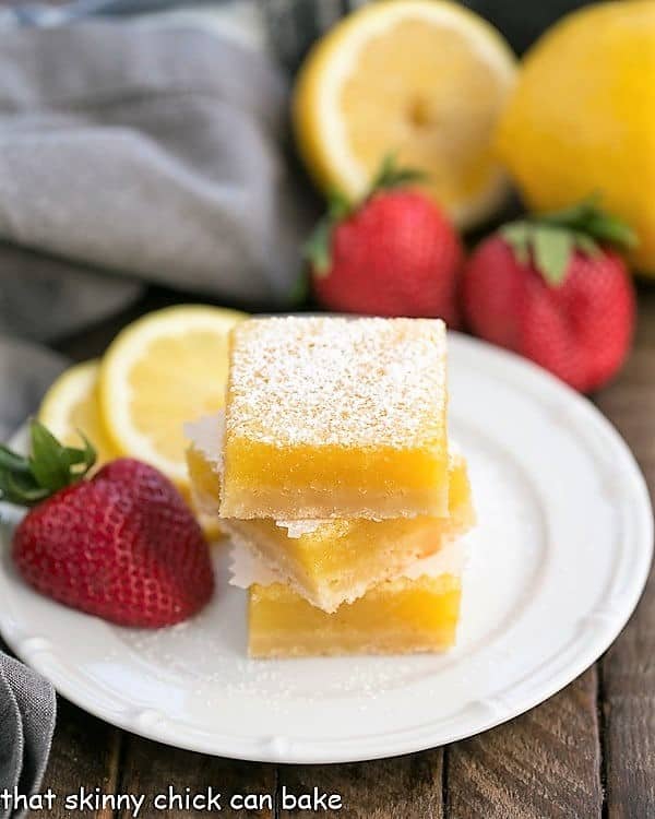 The Best Lemon Bars Recipe - Sweet citrus bars with a delicious shortbread crust! he Best Lemon Bars stacked on a white dessert plate.