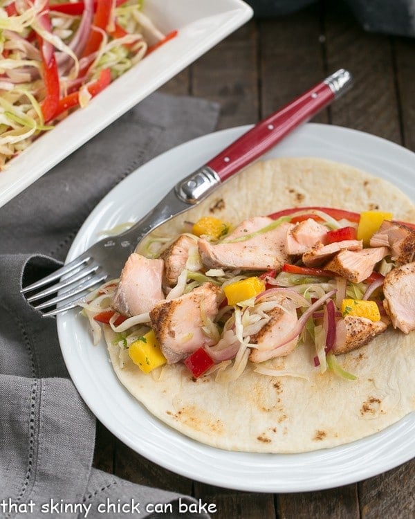 Fish Tacos Recipe with Salmon and Mango Salsa on a round white plate with a red handled fork.
