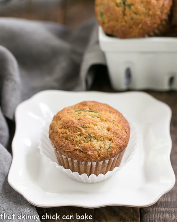 Cinnamon Zucchini Muffins on a white plate with a square basket of muffins in the background.