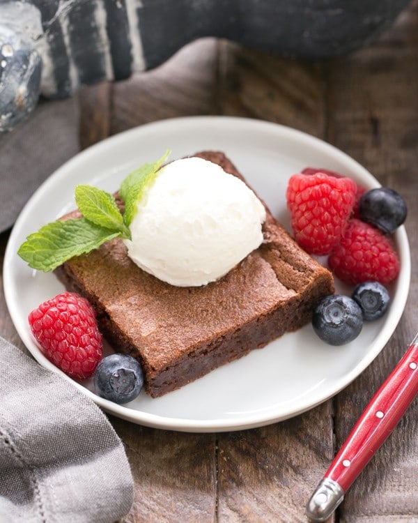 Simple Fudgy Brownies with a dollop of whipped cream and mint sprig on a round white plate.