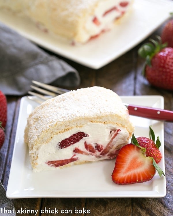 Strawberry Filled Meringue Roulade - A simple baked meringue rolled around strawberries and cream! Strawberry Filled Meringue Roulade slilce on a square white plate with a red handled fork and strawberry garnish