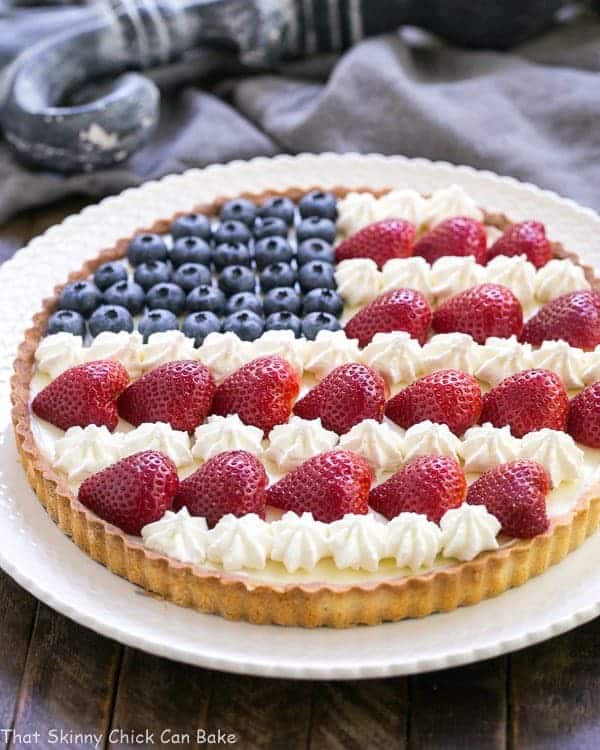 American Flag Fruit Tart - Pate sablee crust, light cream cheese filling and berries and cream stars and stripes! American Flag Fruit Tart on a white serving plate.