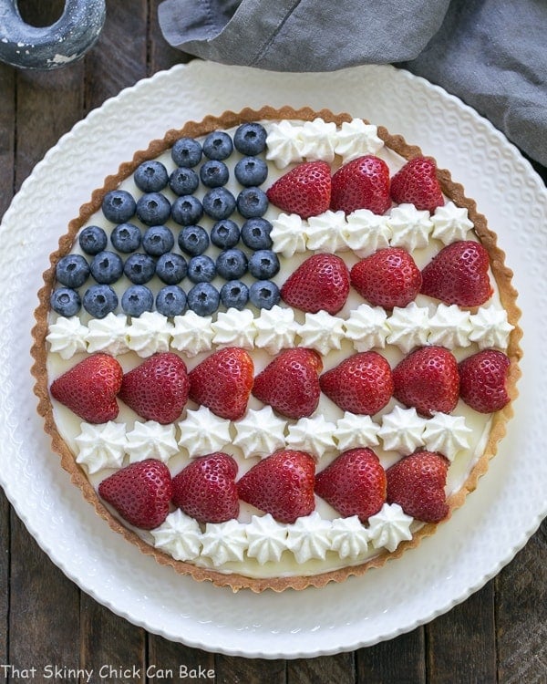 American Flag Fruit Tart - Pate sablee crust, light cream cheese filling and berries and cream stars and stripes! Overhead view of an American Flag Fruit Tart on white serving plate.