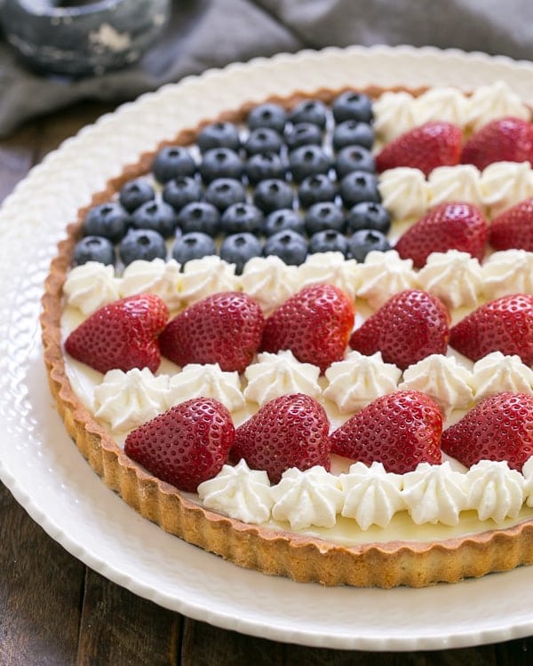 American Flag Fruit Tart - Pate sablee crust, light cream cheese filling and berries and cream stars and stripes! American Flag Fruit Tart on a white ceramic plate.