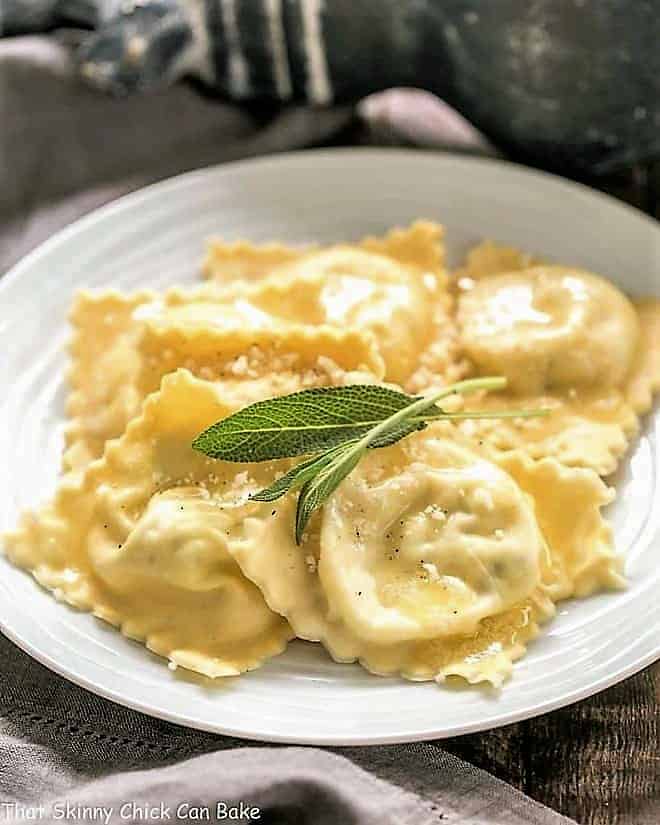 Ravioli on a white plate with sage leaves to garnish.