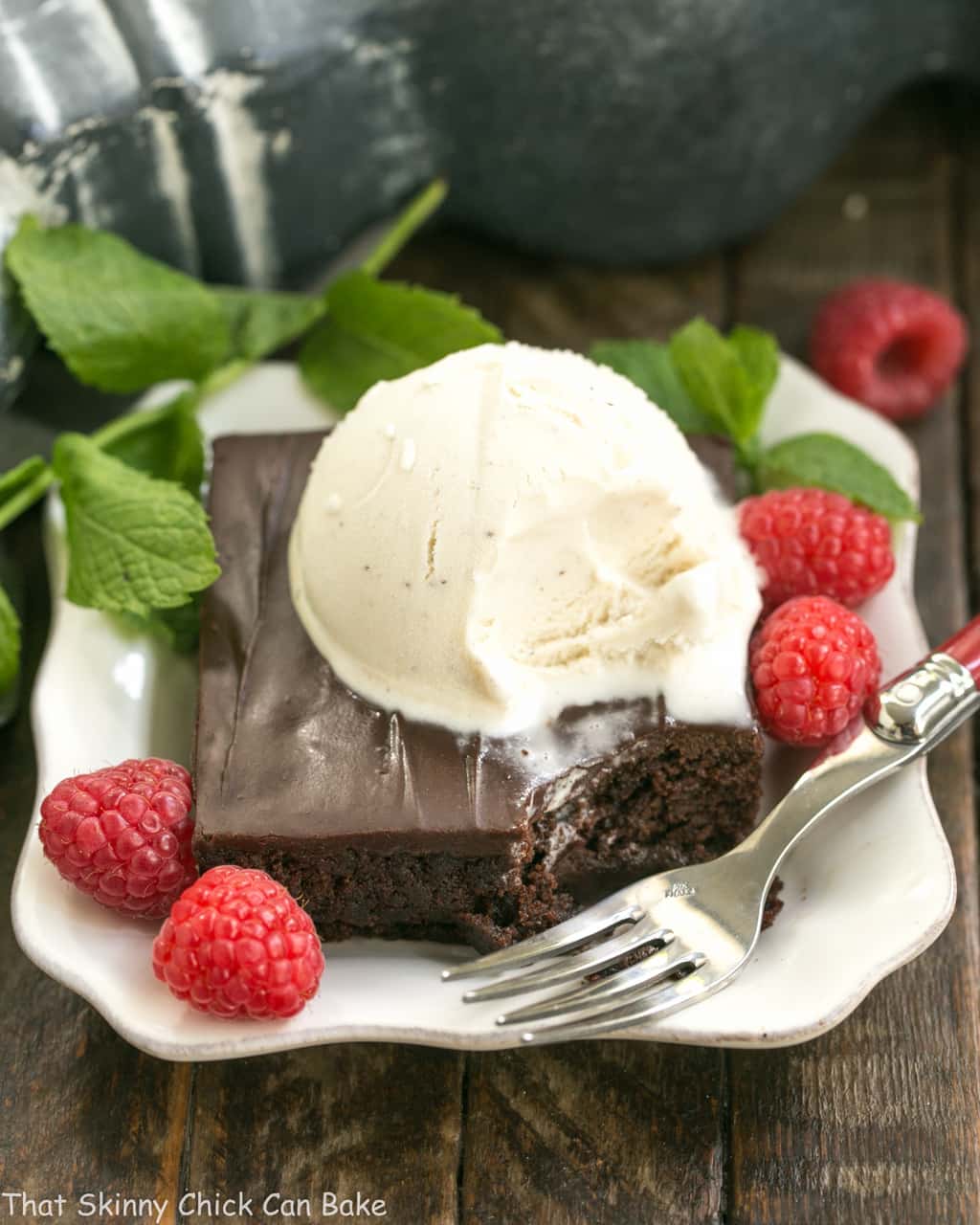 Fudgy Chocolate Sheet Cake with Cocoa Icing on a white dessert plate with ice cream, mint and raspberries.
