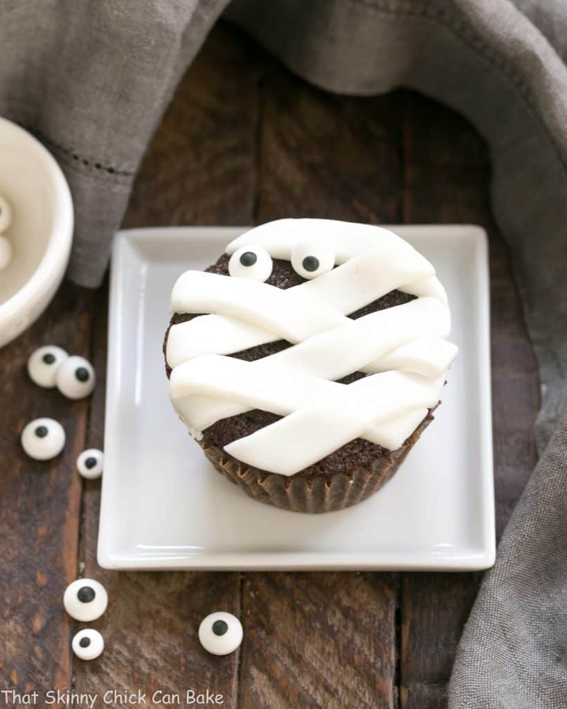 EASY Chocolate Mummy Cupcakes - A simple way to make festive Halloween cupcakes EASY Chocolate Mummy Cupcakes on a square white plate