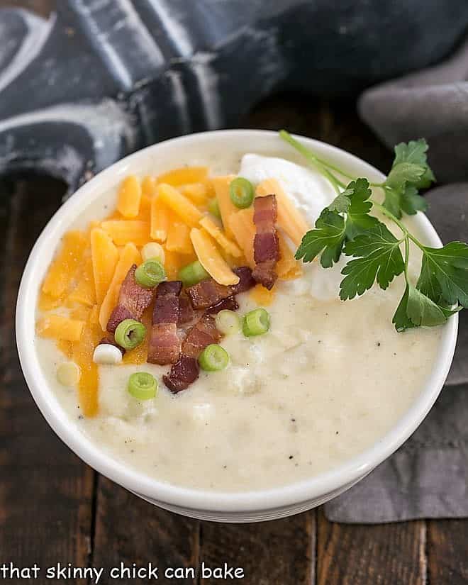 Loaded Baked Potato Soup - Creamy soup with chunks of baked potatoes and topped with cheddar, bacon, sour cream and chives! Loaded Baked Potato Soup in a white bowl with cheese and bacon garnish.