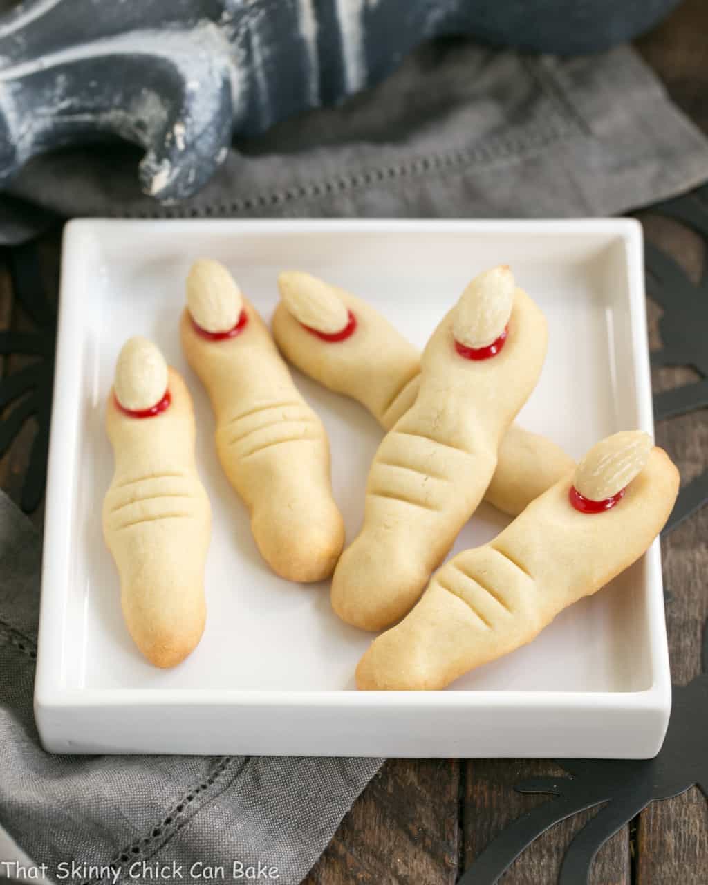 Witches Fingers Cookies - A simple recipe to transform sugar cookie dough into gnarly fingers for Halloween! Witches Fingers Cookies fanned out on a rimmed white square plate.