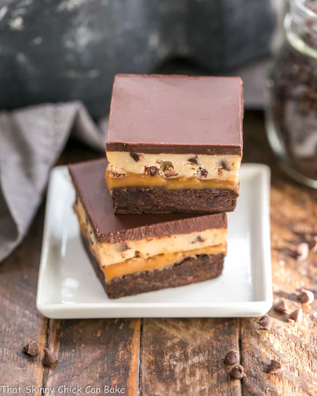 Cookie Dough Billionaire Bars - Layers of brownies, caramel, cookie dough and ganache for an outrageously rich dessert! Cookie Dough Billionaire Bars stacked on a square white plate.