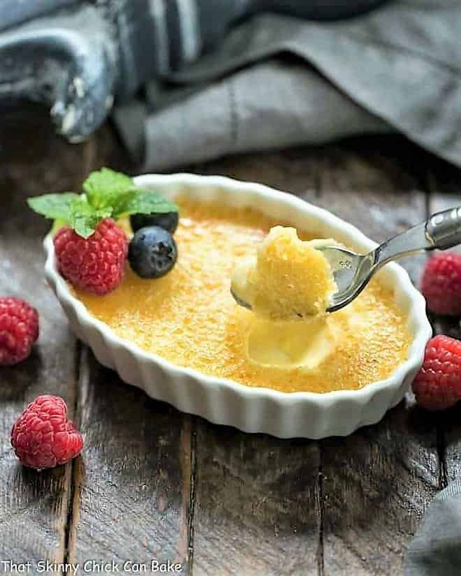 White Chocolate Crème Brûlée - An ultra creamy custard infused with white chocolate and topped with burnt sugar White Chocolate Crème Brûlée in a white ramekin with a spoon.