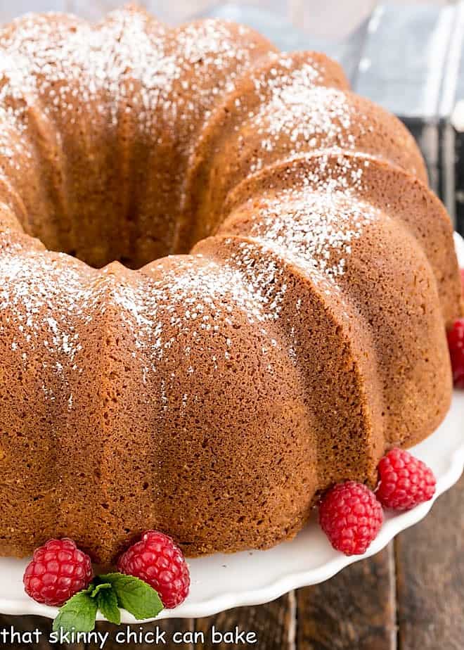 White Chocolate Bundt Cake Flavored with vanilla and a touch of almond, this glazed Bundt cake is a winner! Close view of white chocolate Bundt Cake on a cake stand with raspberries and mint.