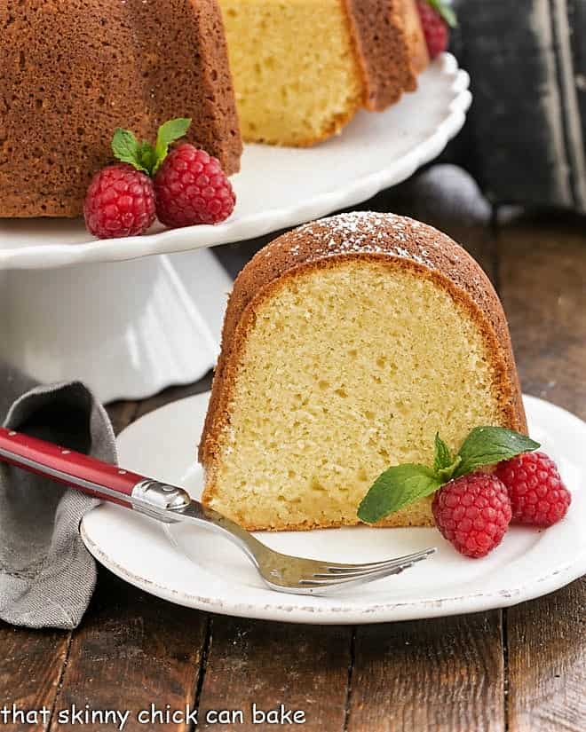White Chocolate Bundt Cake Flavored with vanilla and a touch of almond, this glazed Bundt cake is a winner! slice of white chocolate pound cake on a white plate with raspberries.