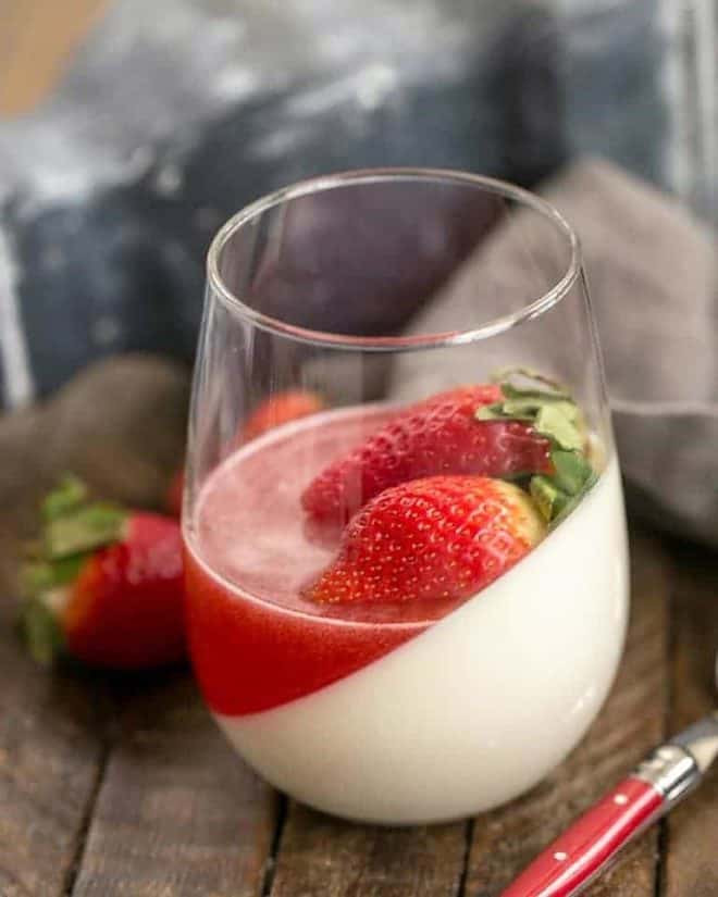 Vanilla Panna Cotta with Strawberry Gelée in a glass topped with fresh strawberries.
