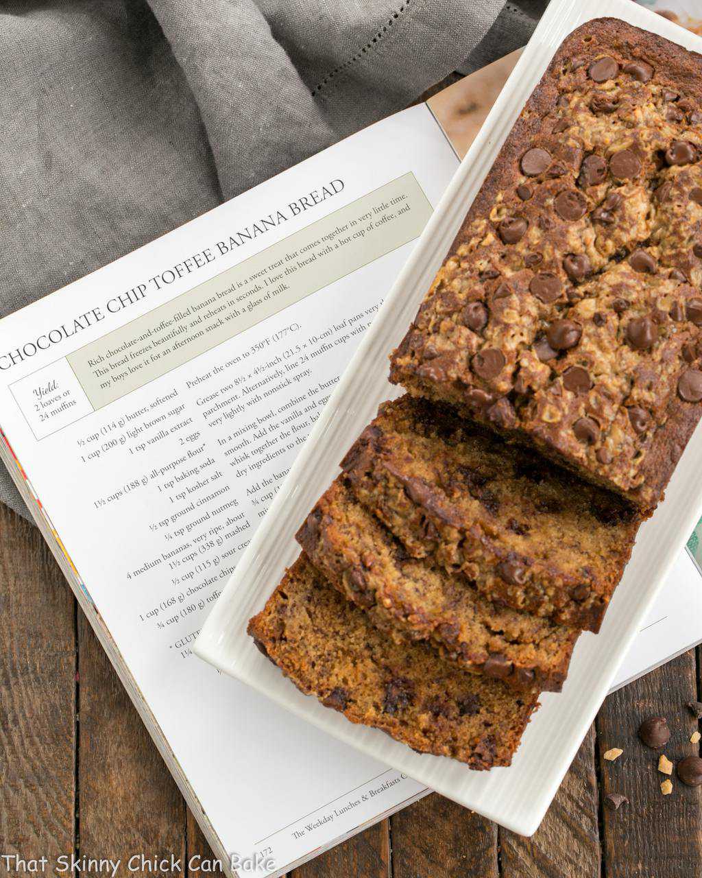 Chocolate Chip Toffee Banana Bread sliced, on a white platter, resting on a cookbook.