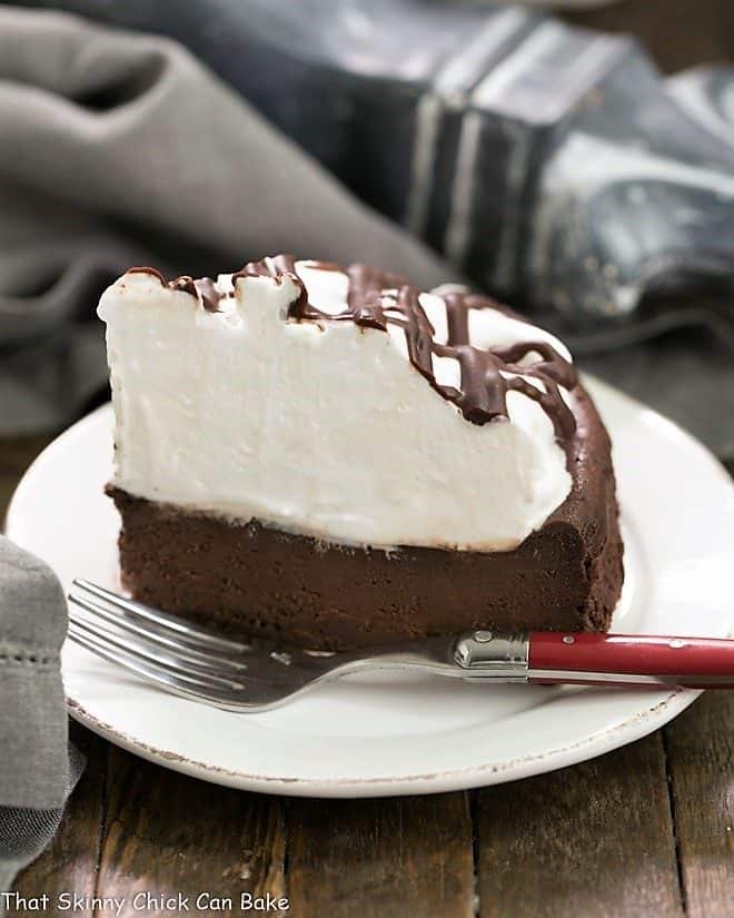 A slice of Flourless Chocolate Cake with Marshmallow Frosting on a white ceramic plate with a red handled fork.