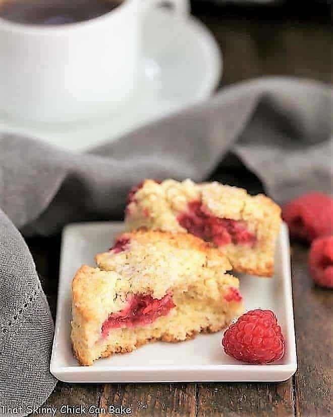Raspberry Scones - terrific, tender scones studded with fresh raspberries. Adding heavy cream is the key to success! Raspberry Cream Scones broken in half on a white plate with a raspberry garnish.