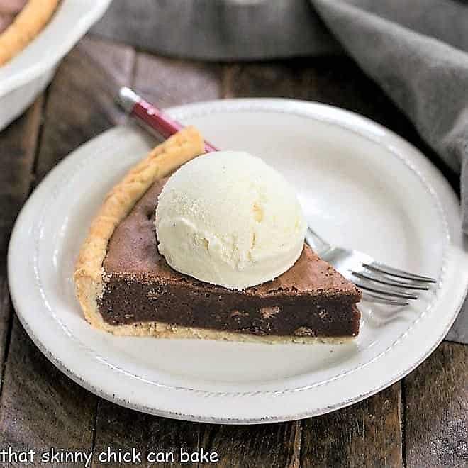 Fudgy Brownie Pie - Rich brownie filling studded with chocolate chips and baked in a flaky pastry shell! Fudgy Brownie Pie wedge topped with ice cream on a white dessert plate.
