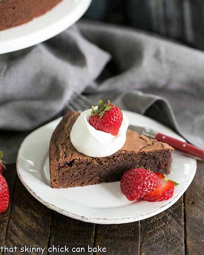 Italian Flourless Chocolate Cake on a white dessert plate with a dollop of cream and strawberries.