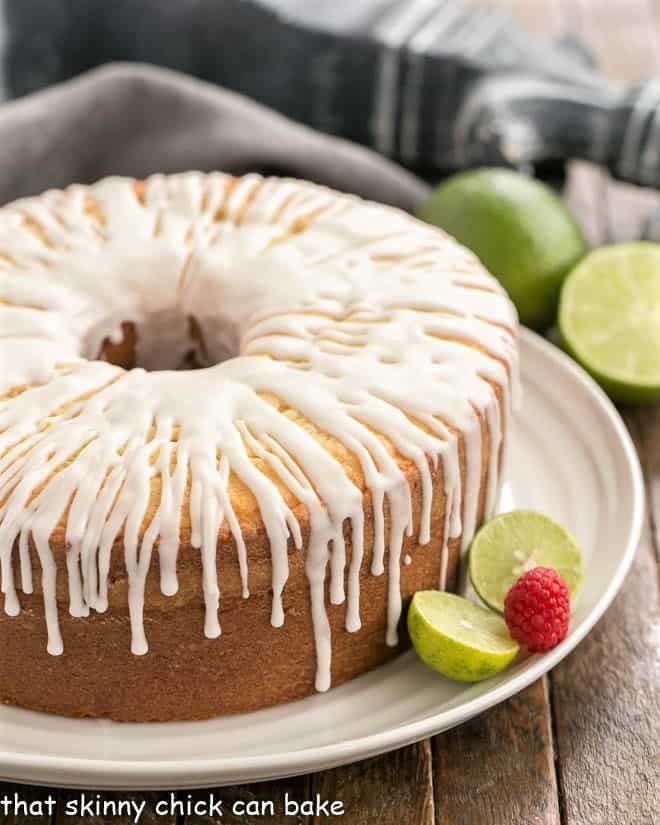 Key Lime Pound Cake - dense, fine crumb cake with a sweet-tart citrusy drizzle A close up of key lime pound cake on a white serving plate garnished with limes and a raspberry.
