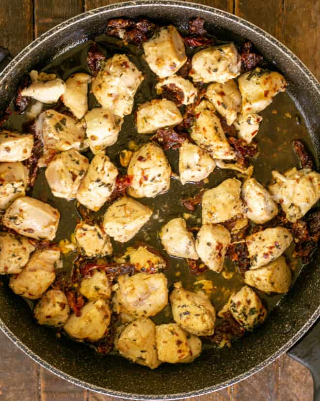 Overhead view Chicken in a skillet with garlic, seasonings and sundried tomatoes.