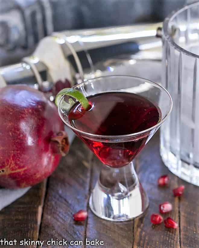 A Pomegranate Cosmopolitan Cocktail in martini glass with a lime twist.