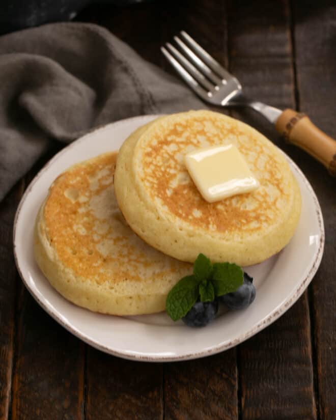 Two buttermilk pancakes on a white plate with a pat of butter.