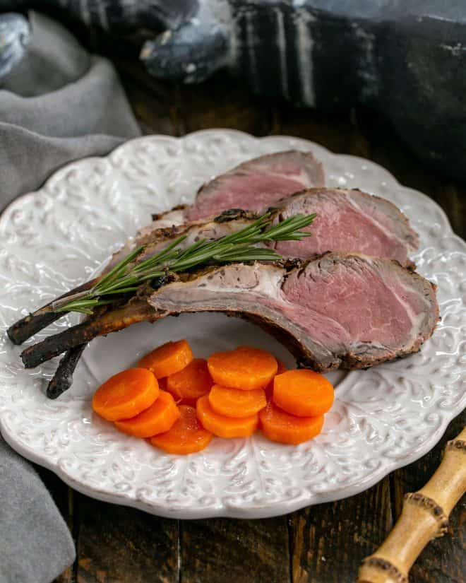 Overhead view of lamb chops on a white decorative plate with a sprig of rosemary and carrot coins.