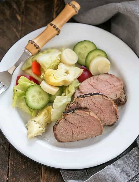 Marinated pork tenderloin sliced on a plate with salad and fork.