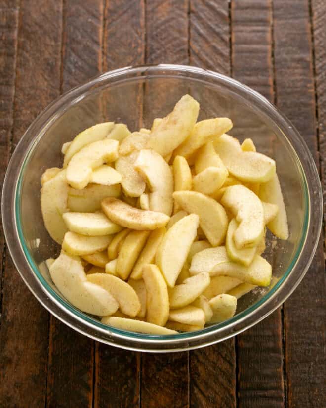 Peeled, sliced, sweetened apples in a glass bowl.
